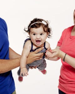Adorable dark haired baby being held between a man and a woman
