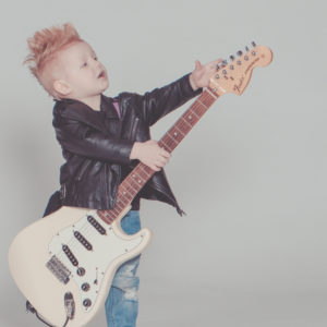 Child with mohawk playing adult sized electric guitar