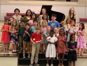 Children holding flowers on stage with teachers behind them