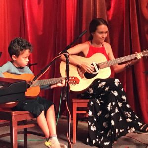 Young woman and a boy on stage playing guitar next to each other