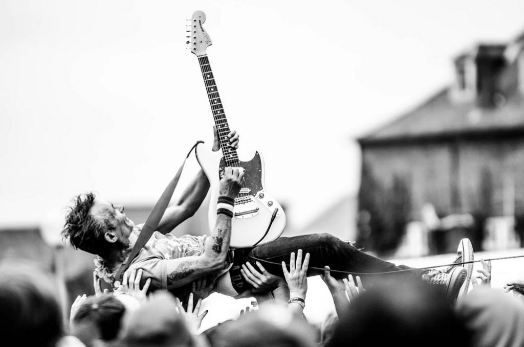 Black and white picture of a man playing an electric guitar in front of a crowd with their hands up