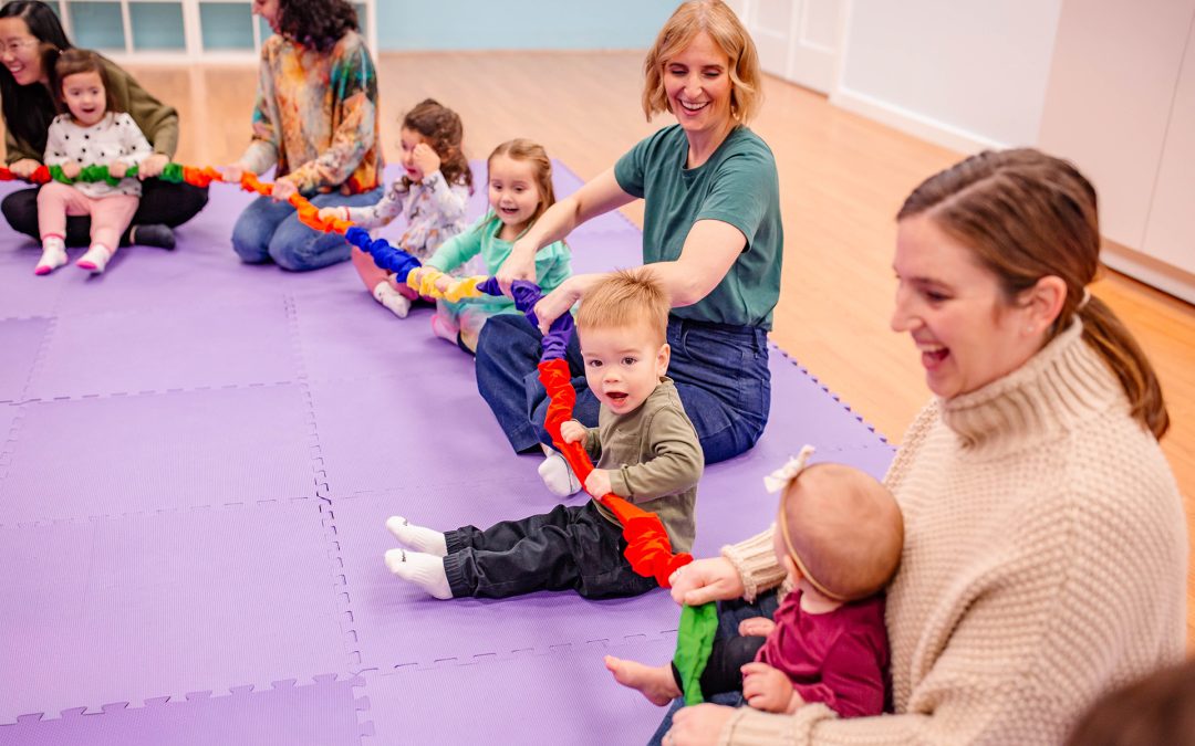 Four mothers with their young children sit in a circle on a purple carpet