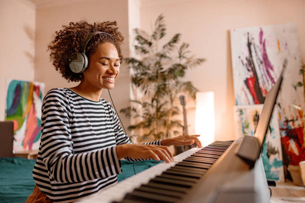 A smiling woman with dark skin and curly brown hair in a striped shirt and headphones playing a digital piano.